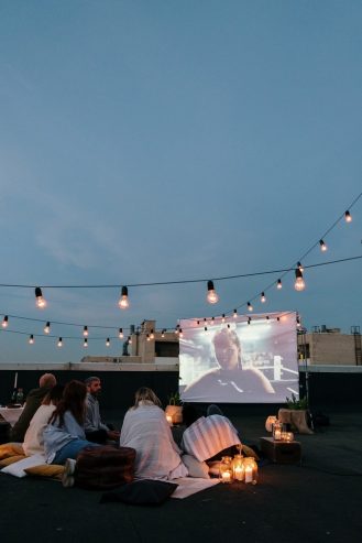 friends watching a movie on an LCD projector screen on top of a building