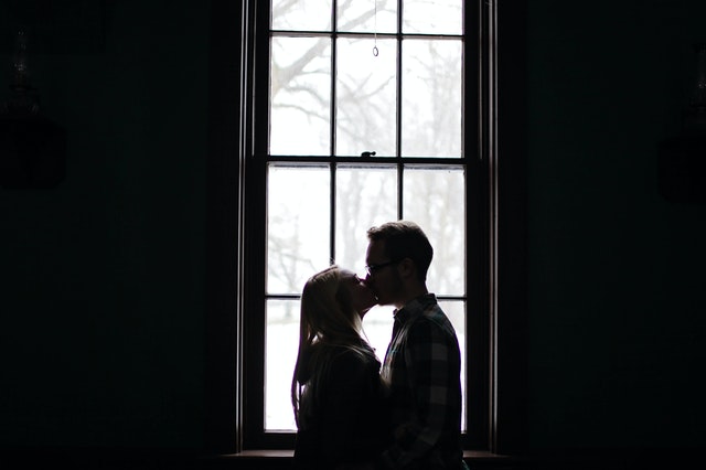 man and woman kissing beside a window