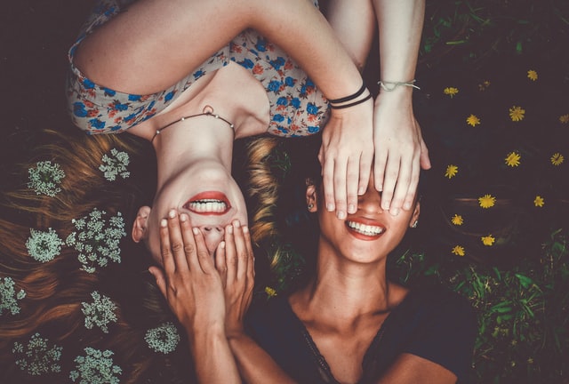 two women covering each other's eyes while lying on the ground 