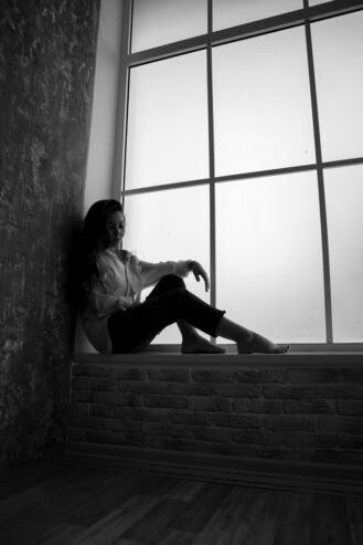 young unhappy woman sitting in solitude near window