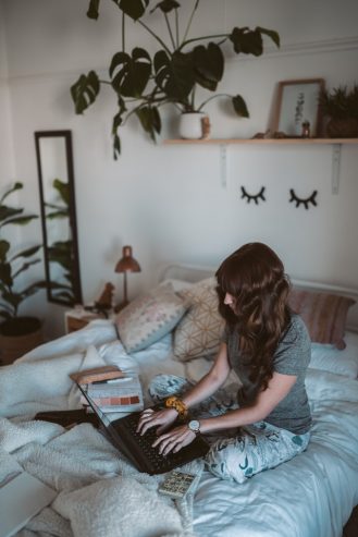 woman sitting on bed checking her laptop