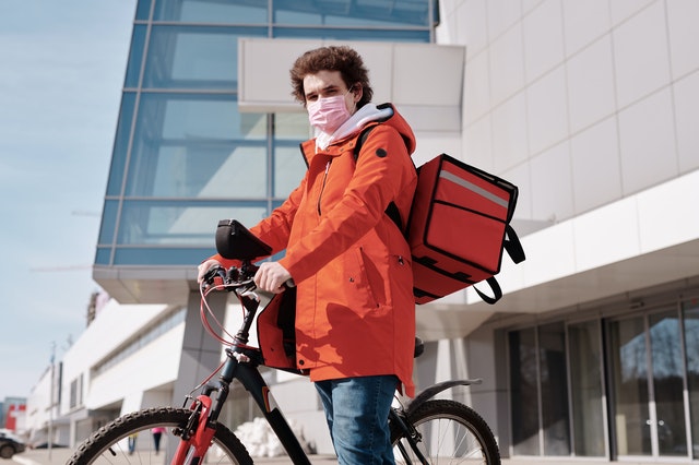 delivery man wearing a face mask and riding a bicycle