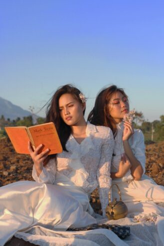 woman reading a book beside another woman holding a flower 